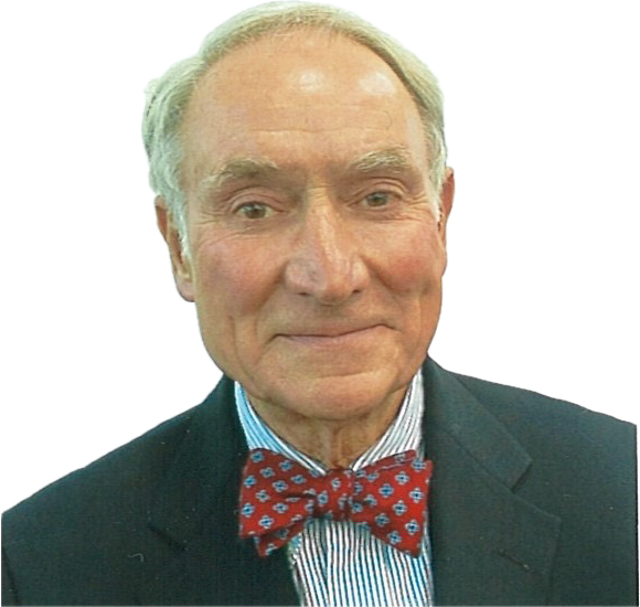 An older man with grey hair is wearing a dark suit, light blue striped shirt, and a red bow tie with a blue pattern. He is smiling slightly and looking directly at the camera. The background is white.